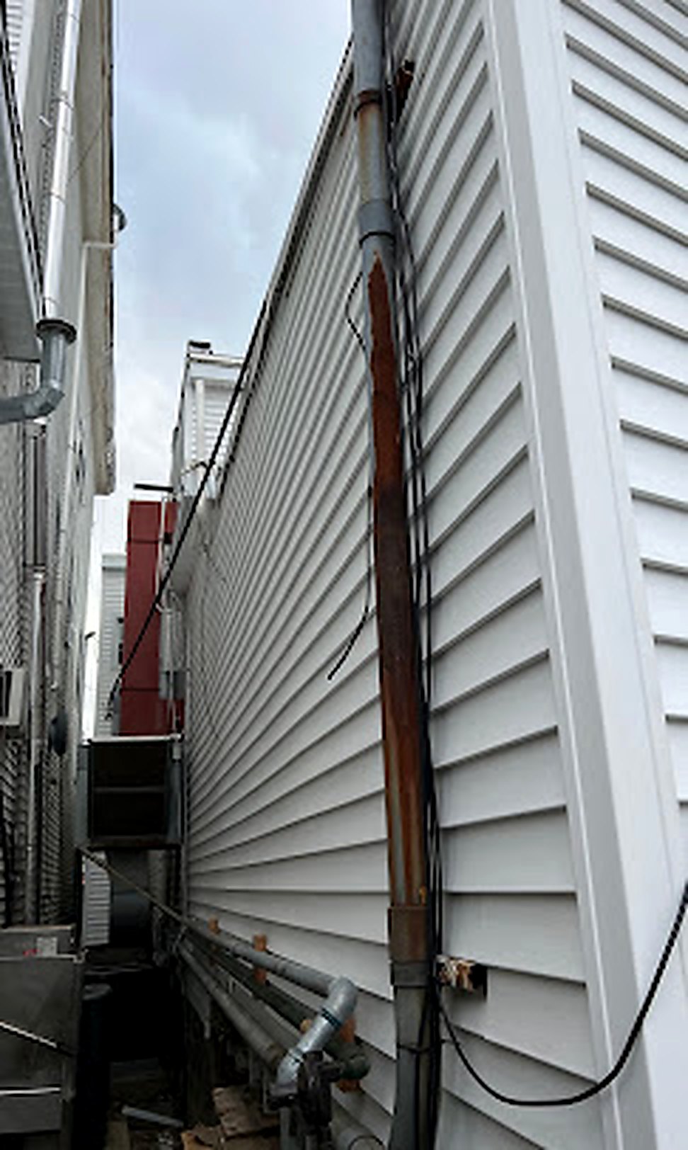 Tall gray vinyl siding wall with utility pipes
